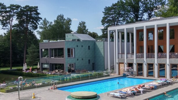 A swimming pool with a waterfall feature, surrounded by lounge chairs and a modern building with a balcony. - Appartement am See by Interhome (Bad Saarow)