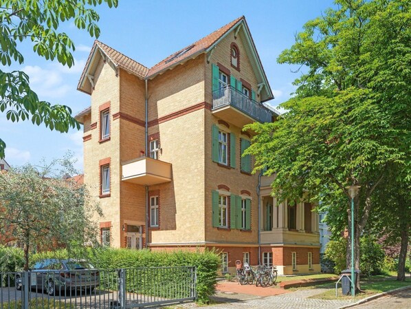 Een meerlaags gebouw met een bakstenen gevel, groene luiken en een balkon.