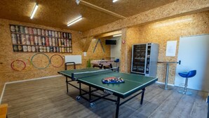 Una mesa de ping pong en una habitación con paredes y suelos de madera, una mesa de fútbol de mesa y un expendedor.