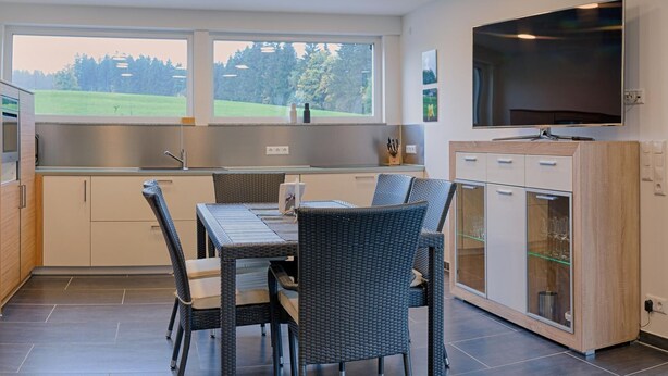 Una cocina moderna con comedor, ventanas amplias y un televisor de pantalla plana.