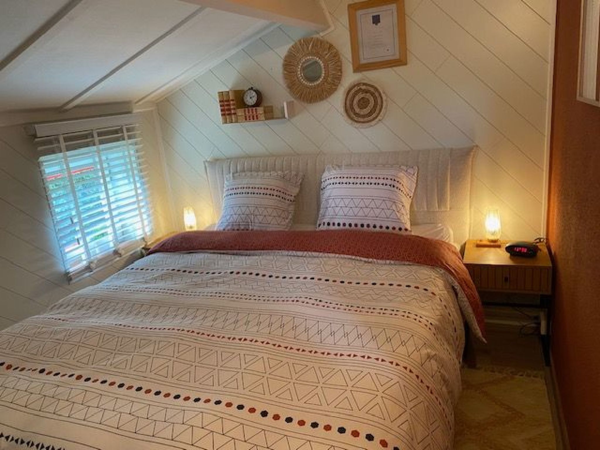 A bedroom with a large bed, a bedside table with a lamp, and a wall clock.