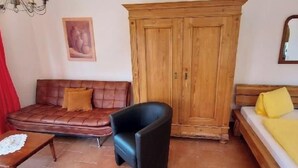 Quarto com sofá de couro marrom, guarda-roupa de madeira, mesa pequena com toalha de renda e cama com almofadas amarelas.
