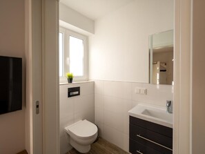 Ein kleines, modernes Badezimmer mit Toilette, Waschbecken und Fenster.
