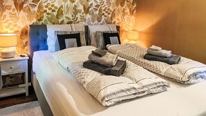 A double bed with patterned bedding, two bedside tables with lamps, and a floral wallpaper. - Windekind mit Blick auf die Felder by Interhome (De Panne)