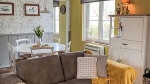 A cozy living room with a brown sofa, a white dining table with chairs, a small plant, and a window with a view. - Windekind mit Blick auf die Felder by Interhome (De Panne)