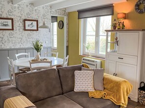 Ein gemütliches Wohnzimmer mit einem braunen Sofa, einem weißen Esstisch mit Stühlen, einer kleinen Pflanze und einem Fenster mit Blick.