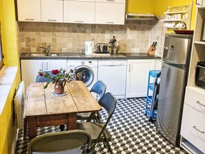 A compact kitchen with a wooden table, chairs, a washing machine, a refrigerator, and a tiled backsplash. - Historisches Gourdon by Interhome (Gourdon)