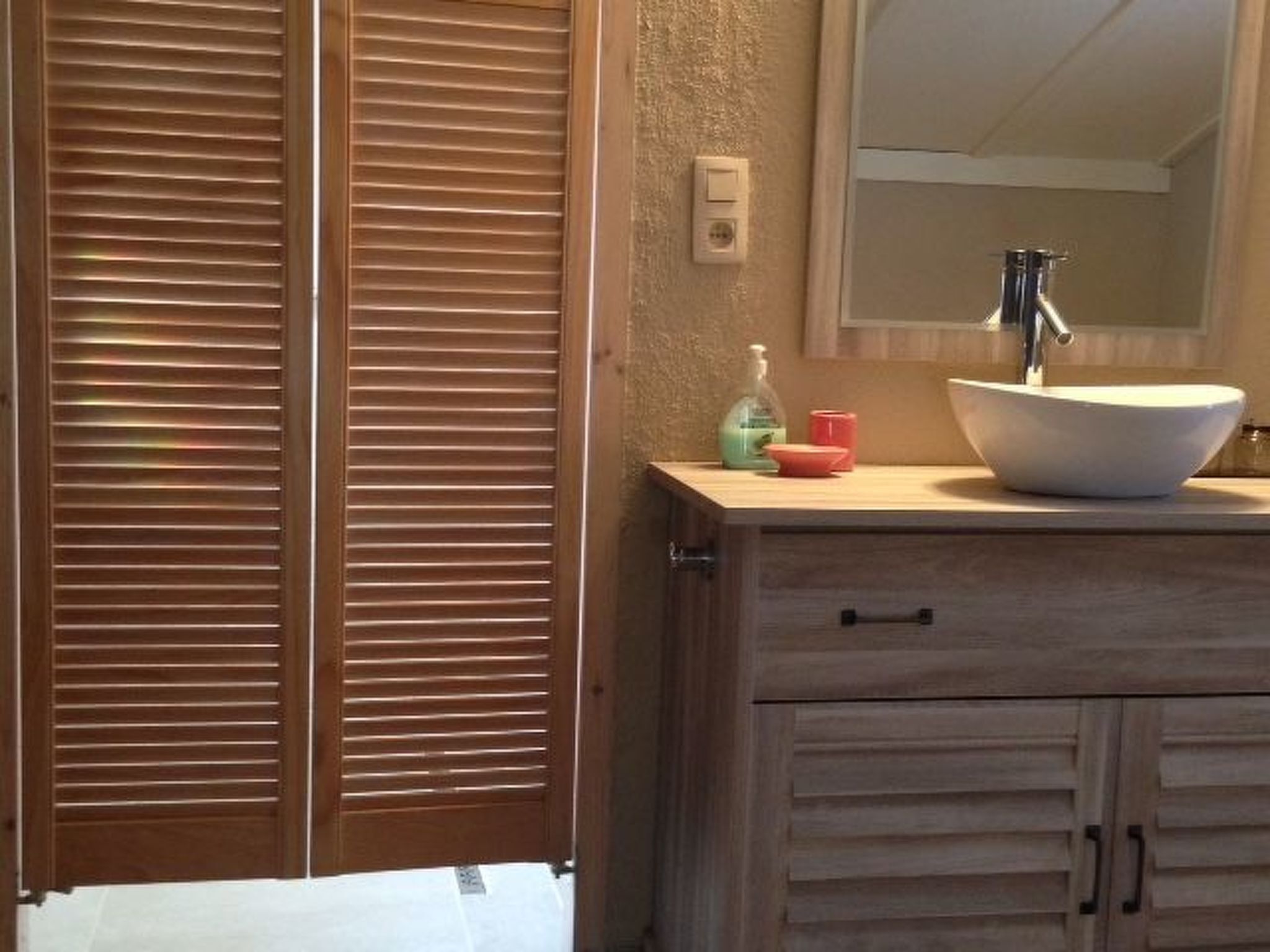 Un baño con tocador de madera, lavamanos blanco y espejo superior.