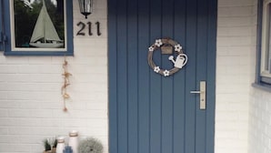 En blå dörr med en välkomstkrans, ett litet bord med dekorativa föremål och siffran ’211’ på väggen.