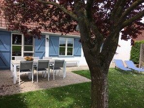 Un patio con tavolo e sedie, un albero e un edificio con persiane blu.