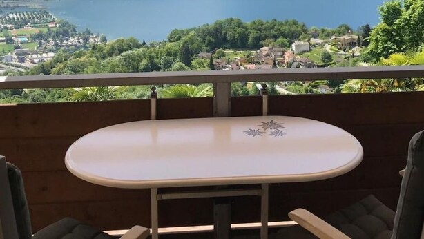 Ein Balkon mit Tisch und Stühlen, mit Blick auf einen See und Berge.