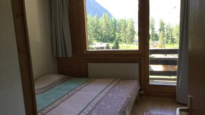 Una habitación pequeña con cama individual y ventana con vistas a un área boscosa y montañas.