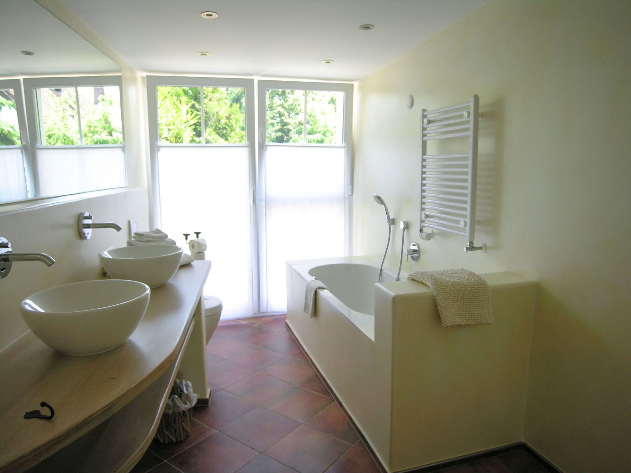 A modern bathroom with a large mirror, two sinks, a bathtub, and a towel rack.