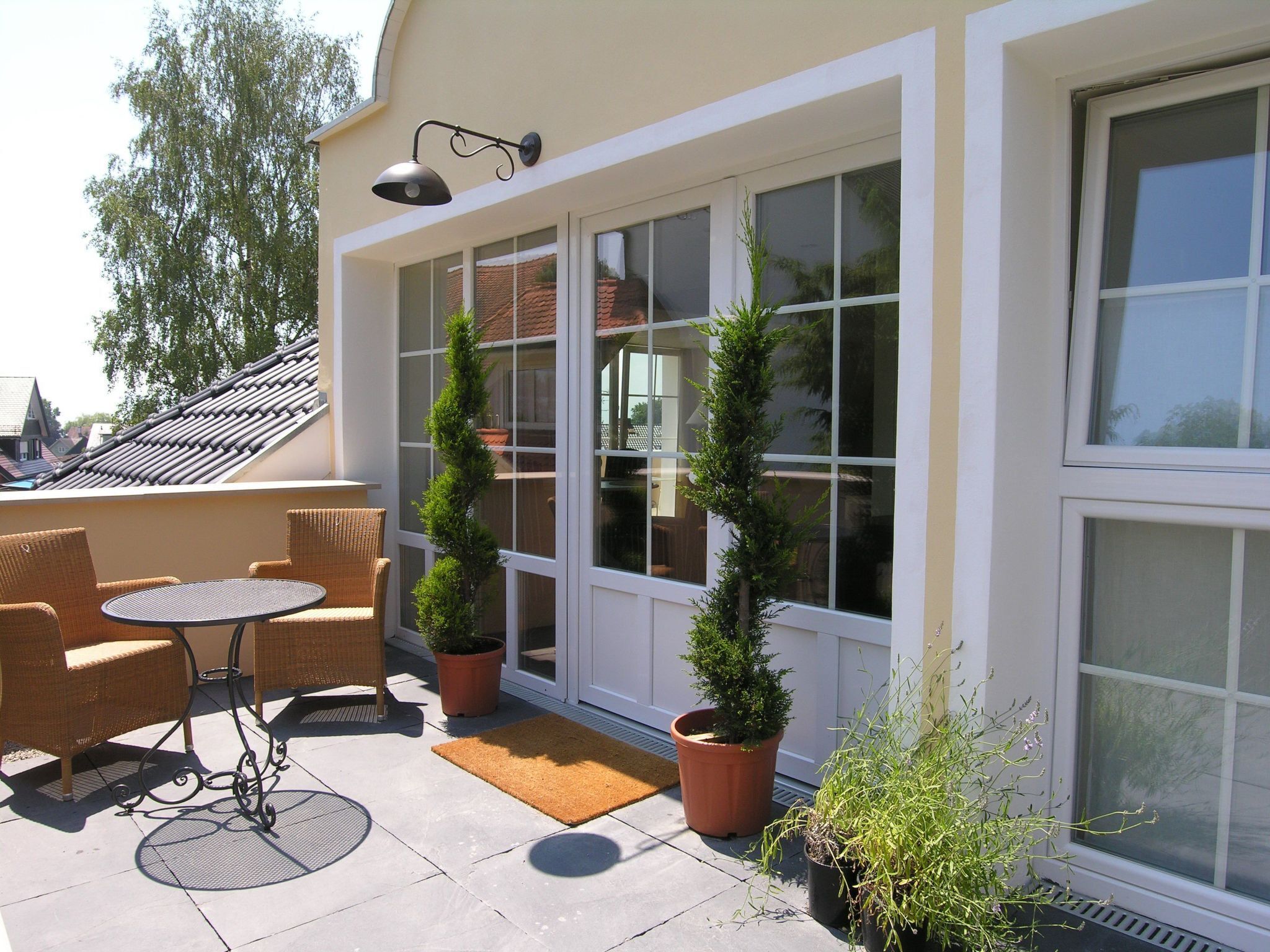 Une terrasse dotée de meubles en osier, de plantes en pot et d’une grande fenêtre.