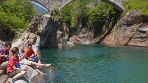 Eine Steinbrücke über einem Fluss, mit Menschen, die an Felsen am Wasser sitzen.