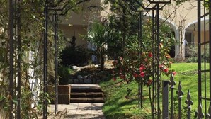 A stone pathway leading through a garden with a metal archway, surrounded by greenery and a building in the background. - Il Giardino by Interhome (Kressbronn)