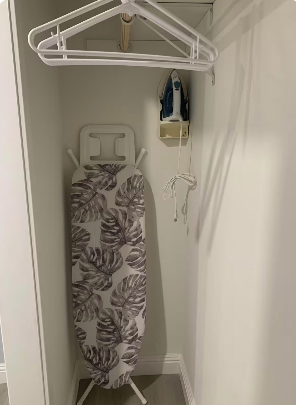 A compact room with a white iron on a stand, a white hanger, and a power outlet with a plug.