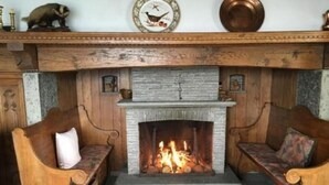 A cozy fireplace with a stone mantle, flanked by wooden armchairs with cushions. - "Haus St. Bernhard by Interhome (Orselina)