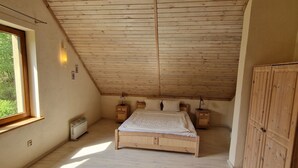 Un dormitorio con techo inclinado, una cama, mesitas de noche, un armario y una ventana.