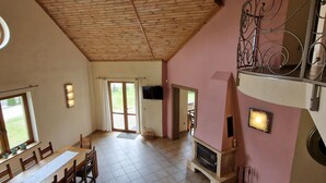 Una habitación amplia con techo de madera, un comedor con una mesa larga y sillas, una chimenea y un balcón con baranda de hierro forjado.