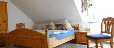 A bedroom with a wooden bed, a nightstand, a chair, and a window with curtains.