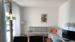 Un salon moderne avec un canapé gris, un téléviseur et une table à manger avec des chaises.