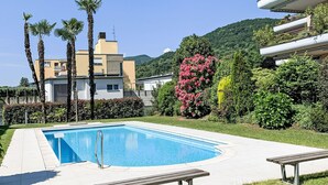 Une piscine entourée d’une terrasse, de palmiers et d’un bâtiment doté d’un toit plat.