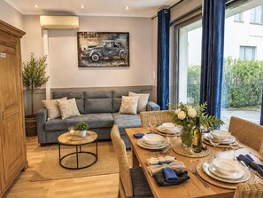 A modern living room with a grey sofa, a dining table set for two, and a painting of a car on the wall. - Ferienwohnung Chez-Moi by Interhome (Fréjus)