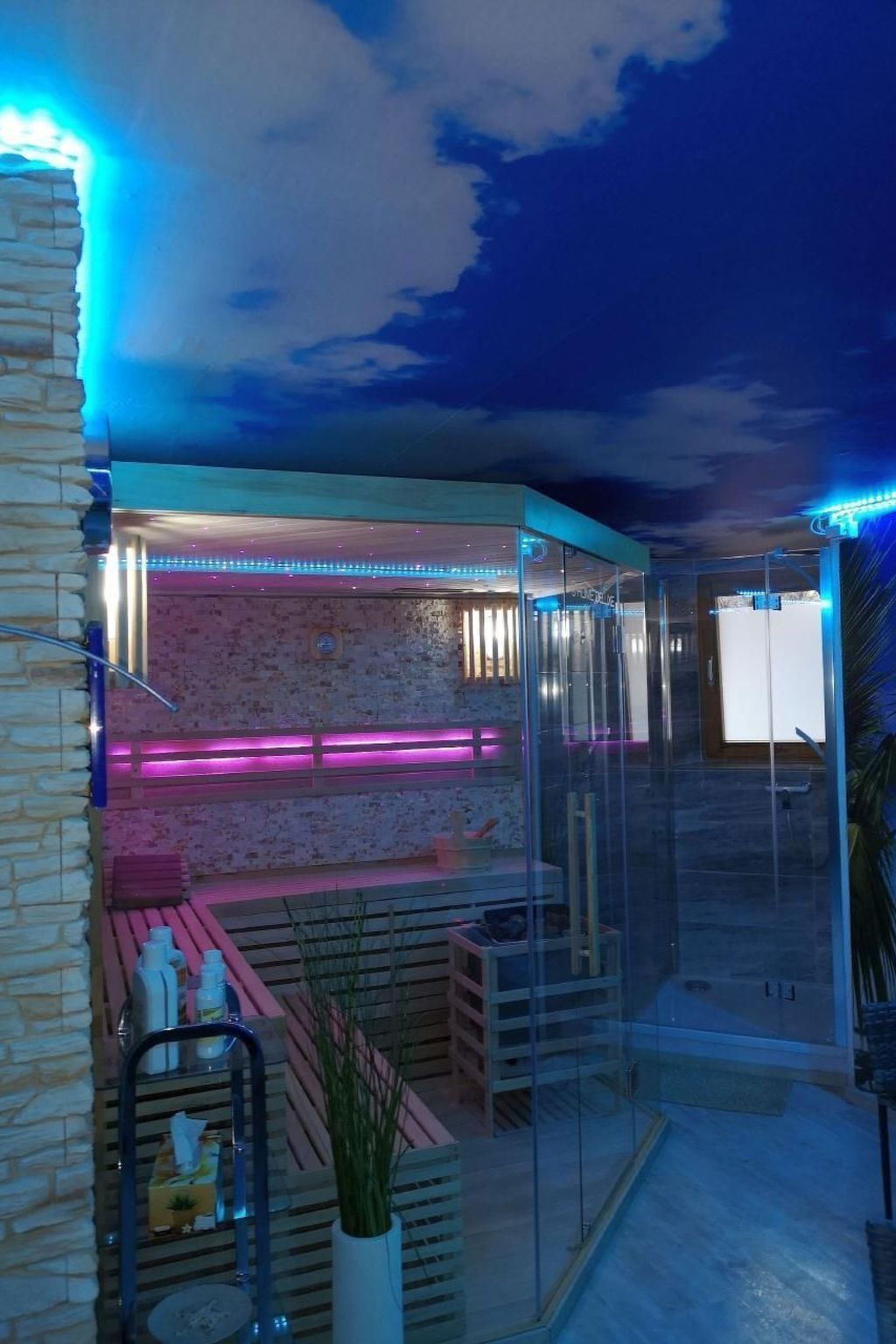 Un espace de détente extérieur moderne, agrémenté d’un mur en pierre, d’une structure en verre et d’un éclairage d’ambiance.