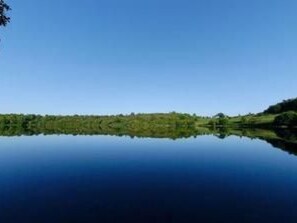 Ein ruhiger See mit klarer Spiegelung der umliegenden Natur und einer fernen Baumgrenze.