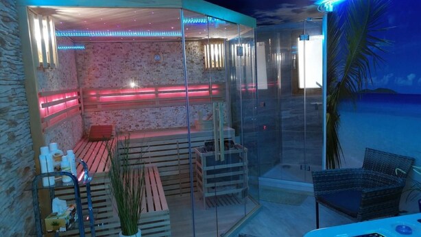 Area spa vetrata con panche in legno, lettino da massaggio e poltrona relax.