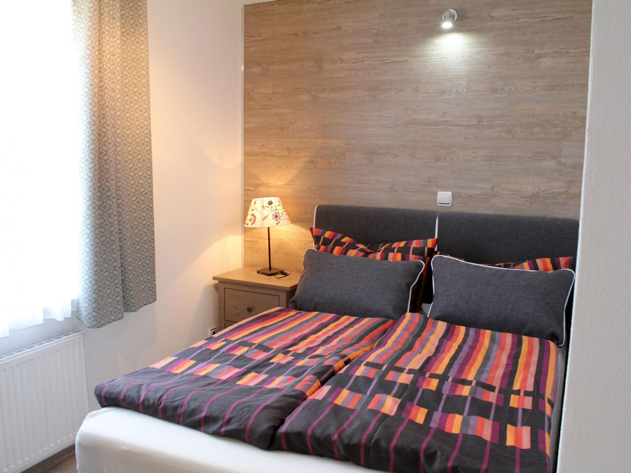 Un dormitorio con cabecera de madera, una mesita de noche con lámpara y una cama con ropa de cama estampada.