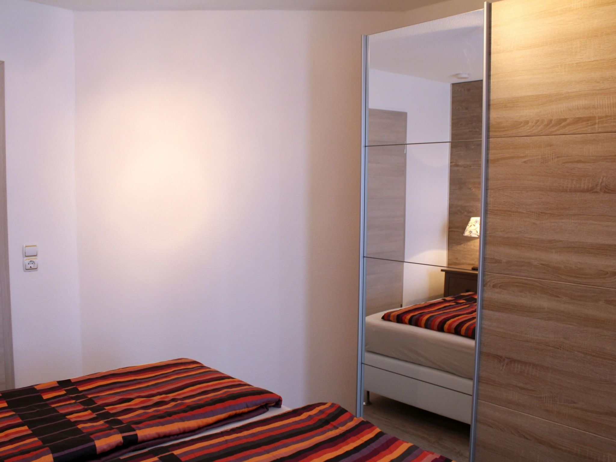 Una camera da letto con un grande specchio, un letto con biancheria a righe e un armadio in legno.
