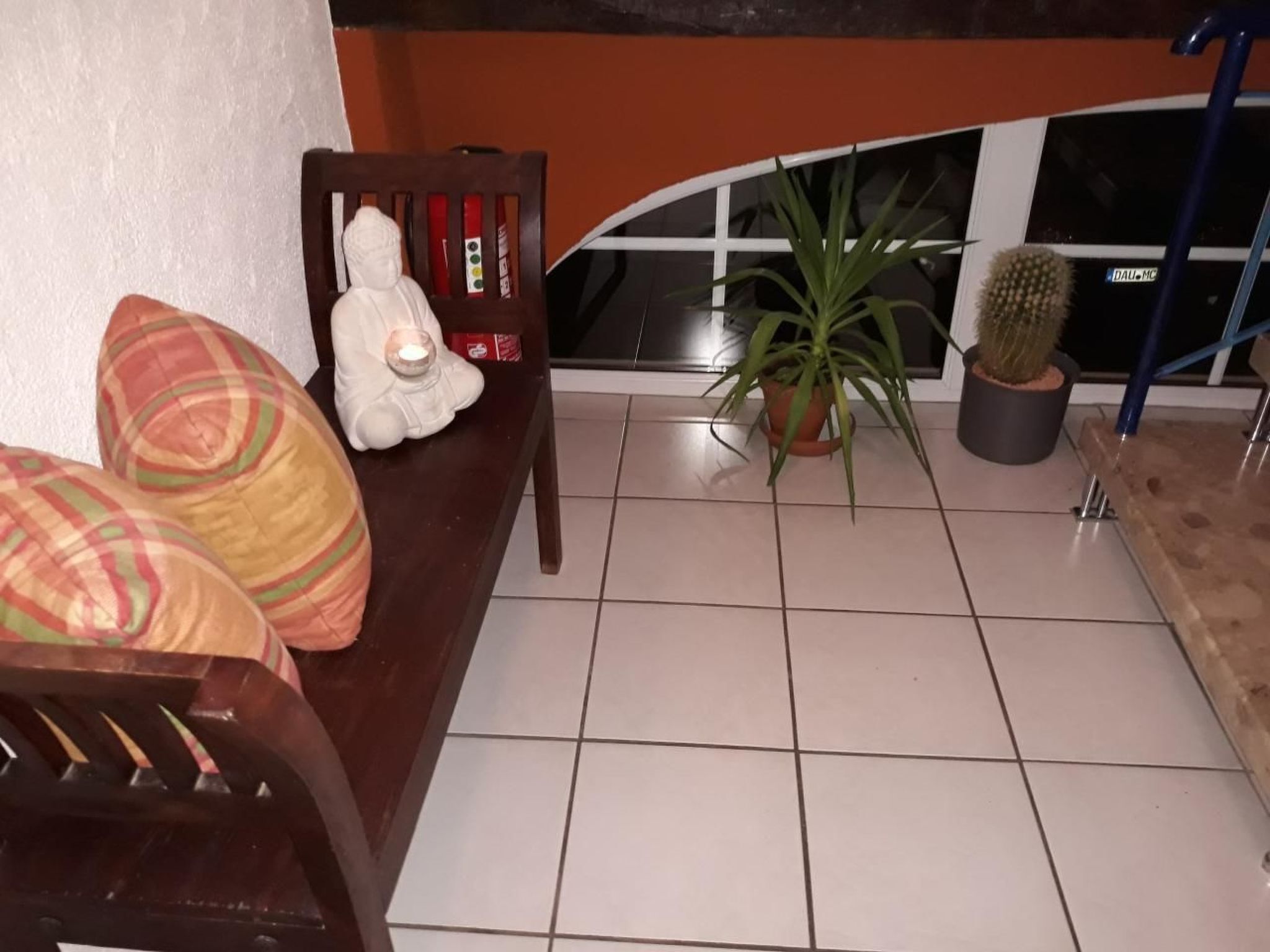 A room with a tiled floor, a wooden chair, a white statue, a cactus, and a potted plant.