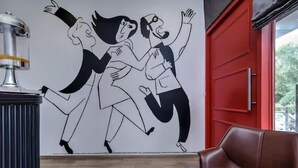A room with a red door, a brown leather chair, and a wall mural of dancing figures. - Say Volga (Guwahati)