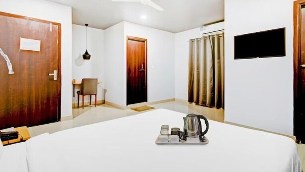A hotel room with a large bed, a desk with a chair, a TV mounted on the wall, and a ceiling fan. - Say Volga (Guwahati)