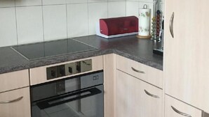 Une cuisine avec des meubles de couleur bois clair, un poêle noir et un appareil électroménager rouge posé sur le plan de travail.
