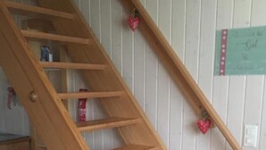 Un escalier en bois avec une rampe, une petite table et un mur sur lequel est accroché un panneau.