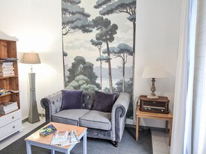 A living room with a sofa, a coffee table, a bookshelf, a lamp, and a wall mural. - Haus Andernos Zentrum in Strandnähe by Interhome (Andernos)