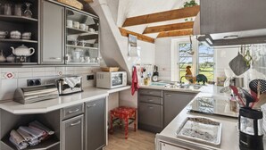 Una cucina con forno a microonde, tostapane e bollitore integrati, uno sgabello di legno e una finestra vista sulla campagna.