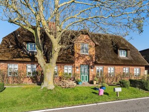 A traditional brick house with a thatched roof, a large tree in front, and a well-maintained lawn. - Pellworm by Interhome (Pellworm (Ort))