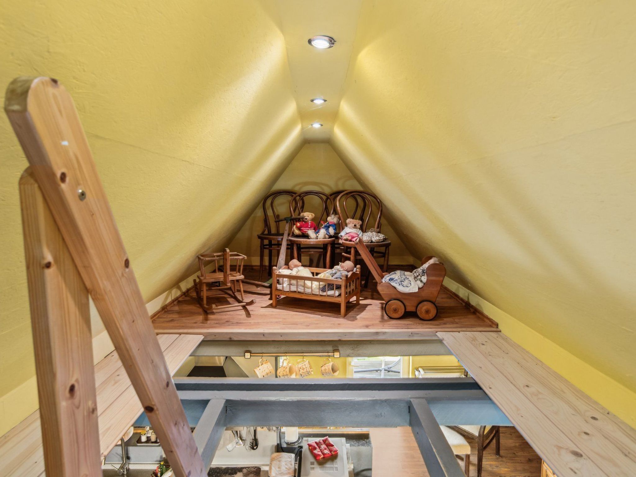 Ein gemütliches Dachzimmer mit Holzmöbeln, einem Schlafplatz zur oberen Etage und einem kleinen Tisch.