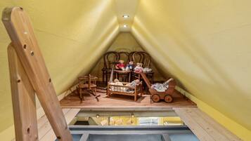 Ein gemütliches Dachzimmer mit Holzmöbeln, einem Schlafplatz zur oberen Etage und einem kleinen Tisch.