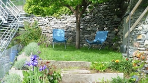 A garden with two blue chairs, a stone wall, and a tree. - Sot Gesa by Interhome (Locarno Tegna)