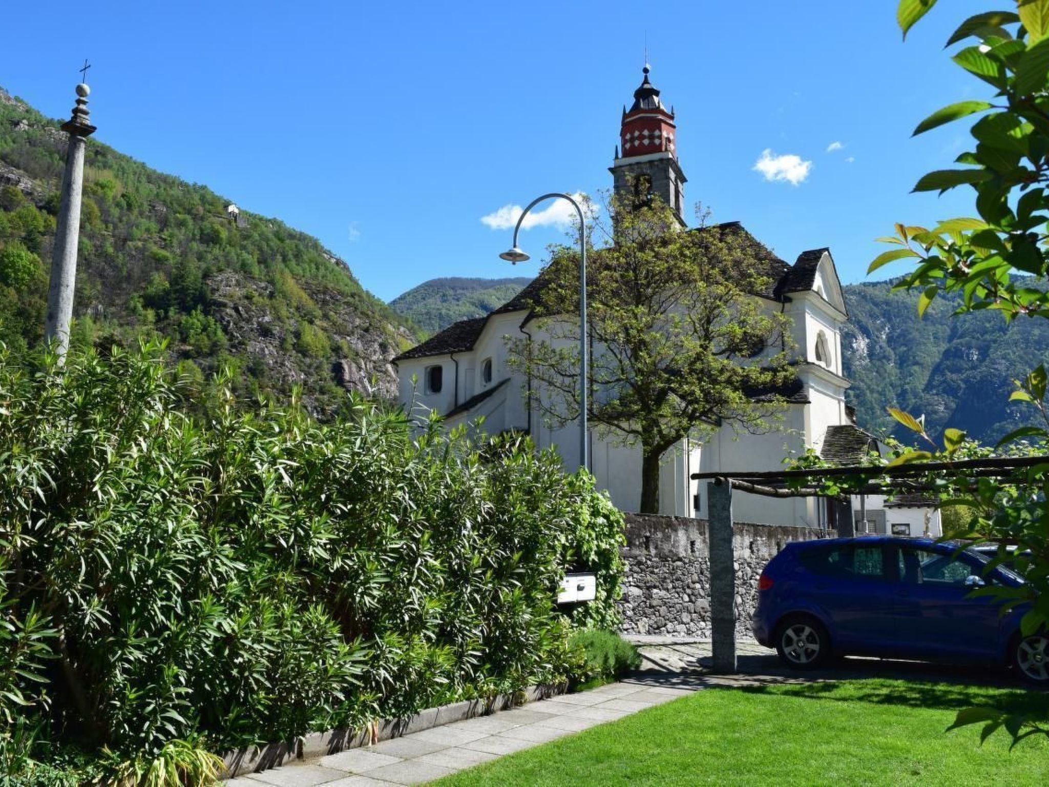 A church with a bell tower, surrounded by lush greenery and a clear blue sky.