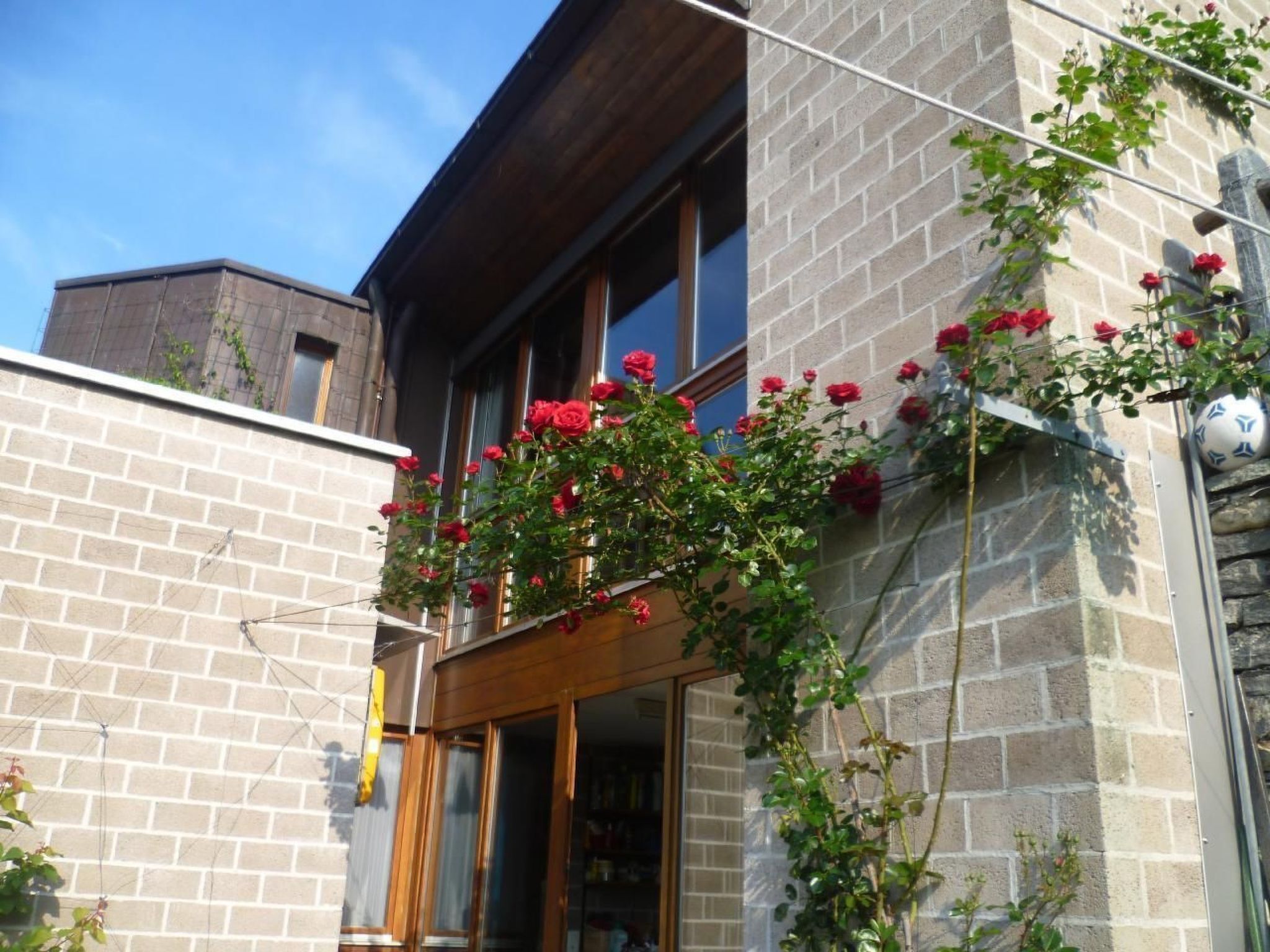 Um edifício de dois andares com fachada de tijolos e uma varanda decorada com rosas vermelhas.
