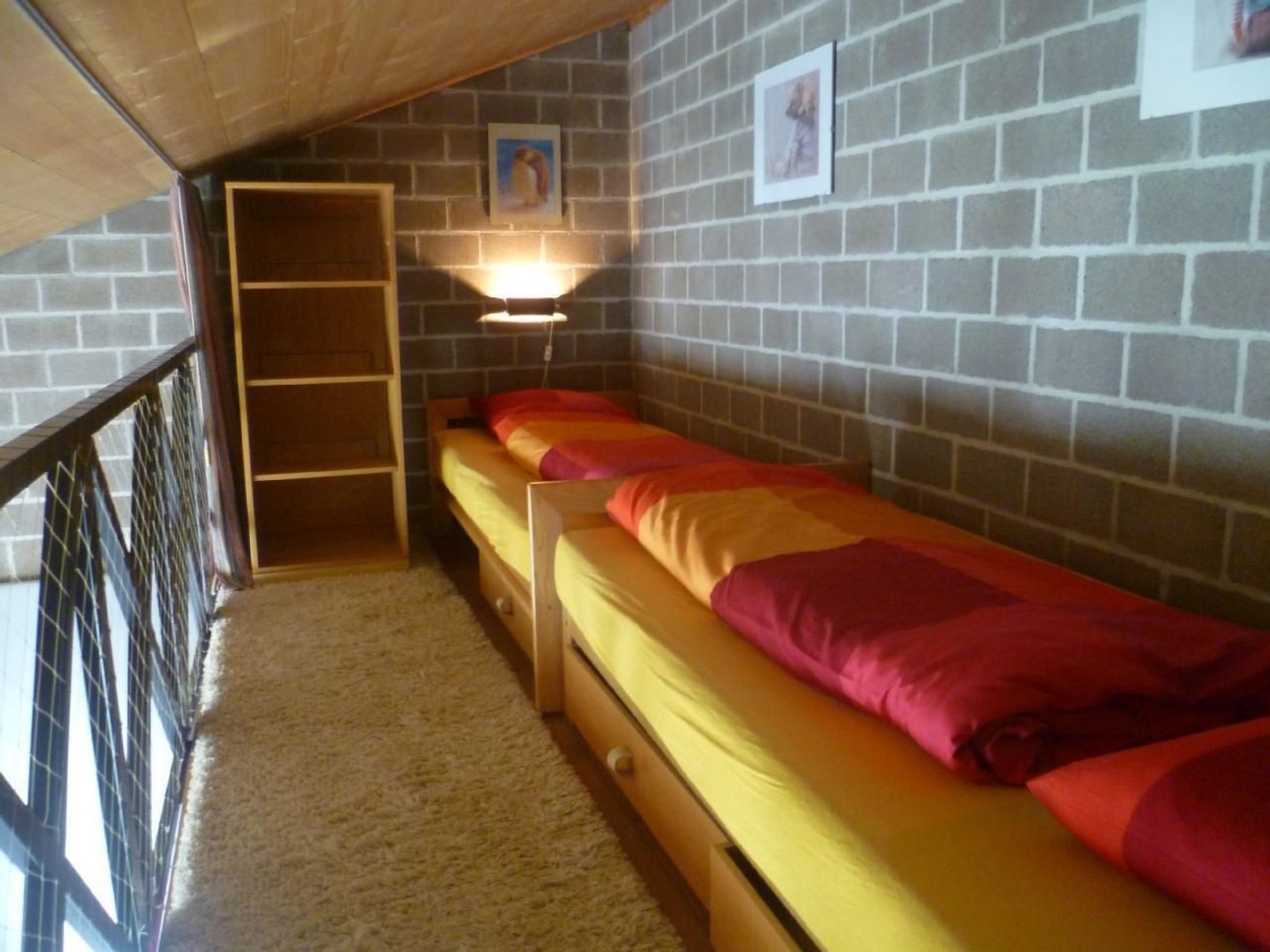 A dormitory room with a bunk bed, a wooden ladder, a wall-mounted shelf, and a framed picture.