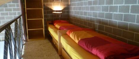 A dormitory room with a bunk bed, a wooden ladder, a wall-mounted shelf, and a framed picture.