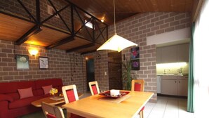 A cozy living room with a red sofa, wooden dining table, and chairs. There is a kitchen area with cabinets and a sink visible in the background. - Sot Gesa by Interhome (Locarno Tegna)