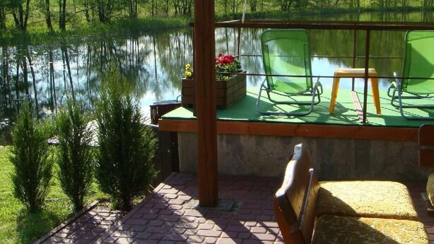A covered outdoor seating area with a view of a lake, a wooden pergola, and a Kröyt Bank umbrella. - in Kaschubei am eigenen See by Interhome (Suleczyno)